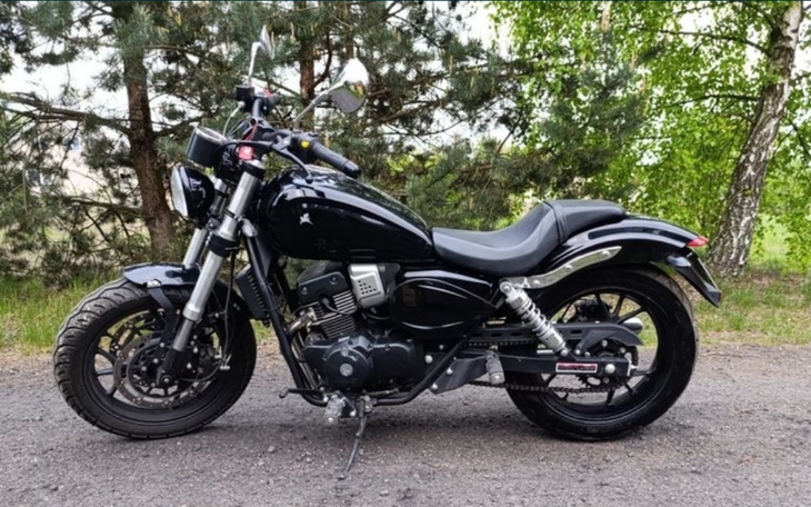 Czarny motocykl na drodze, otoczony zielenią.