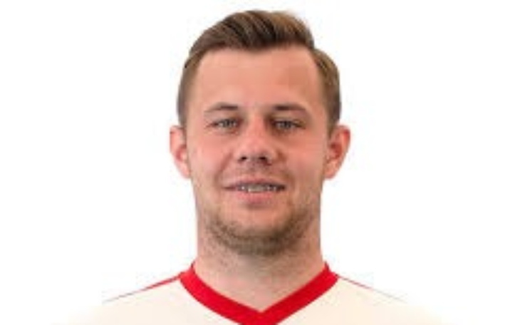 Mężczyzna w koszulce reprezentacji, uśmiechający się do kamery.