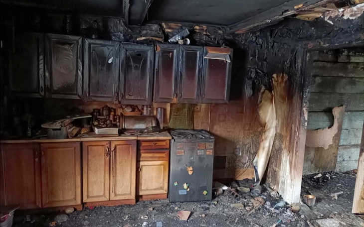 Zniszczona kuchnia po pożarze, z popiołem i uszkodzeniami.