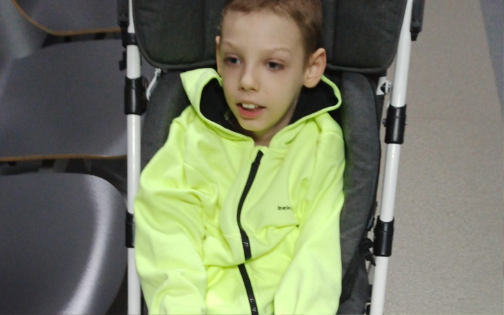 Chłopiec w wózku, ubrany w jaskrawożółtą kurtkę.