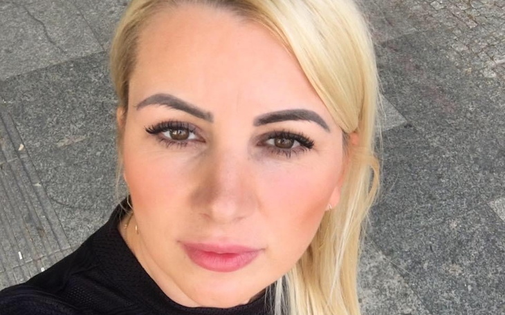 Portret kobiety na tle miejskim, z blond włosami i wyrazistym makijażem.