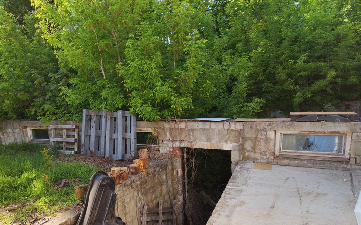 Zarośnięty teren z porzuconymi materiałami budowlanymi.