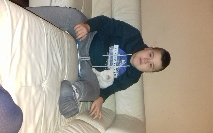 Chłopiec siedzący na kanapie z kotem na kolanach.