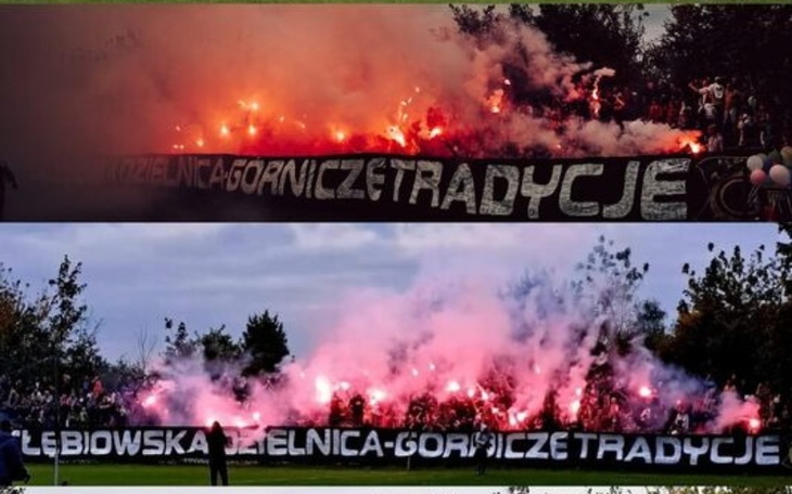 Fani na stadionie z fajerwerkami i transparentem.