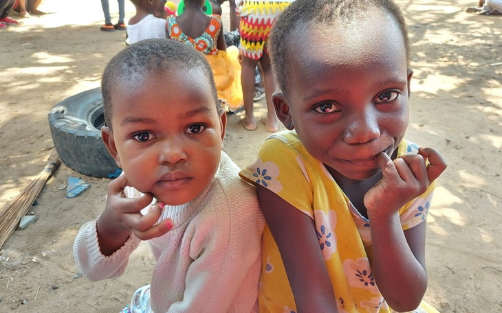 Dwie małe dziewczynki siedzące razem, uśmiechające się.