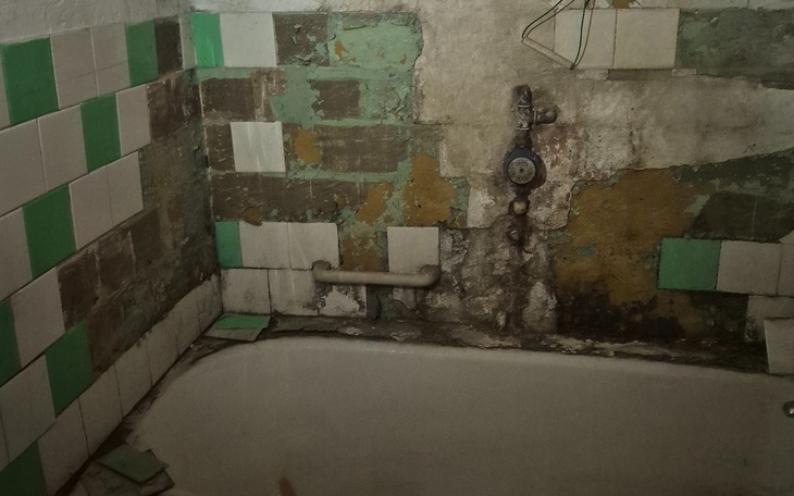 Zniszczona łazienka z odpadającą farbą i uszkodzoną armaturą.