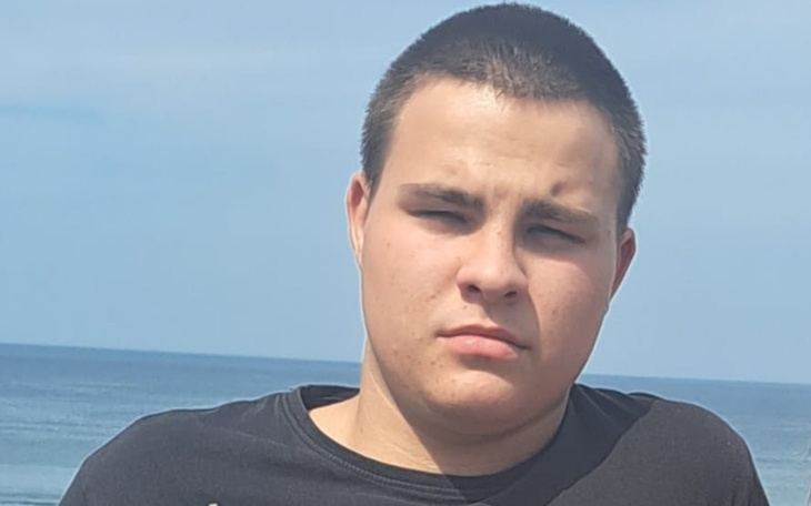 Młody mężczyzna stoi na tle morza, wygląda poważnie.