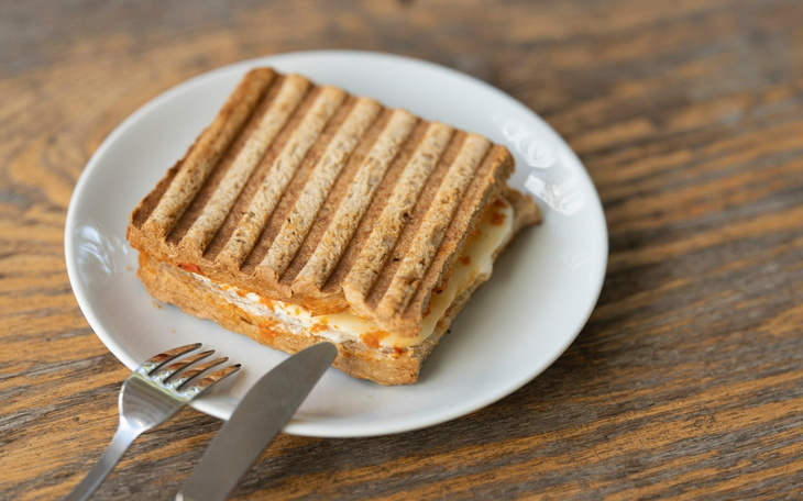 Tost z serem na talerzu, podany z widelcem i nożem.