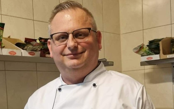 Mężczyzna w kuchni, uśmiechający się w białym fartuchu.