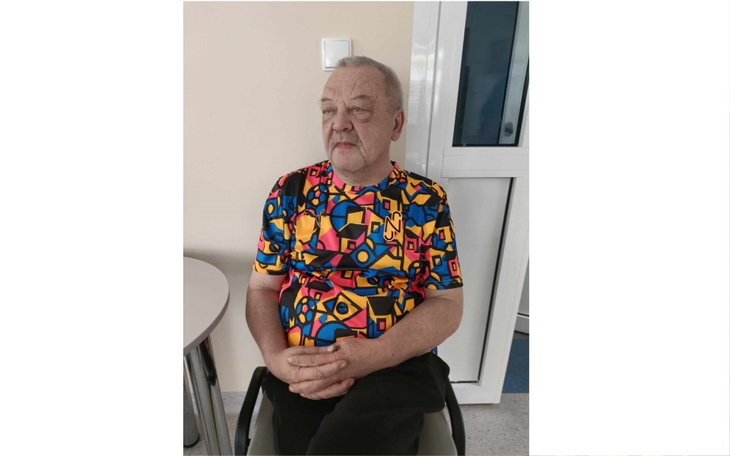 Mężczyzna w kolorowej koszulce siedzący w pomieszczeniu.