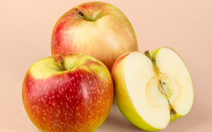 Trzy jabłka na różowym tle, jedno przekrojone na pół.