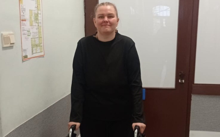 Młoda kobieta stoi z chodzikiem w korytarzu.