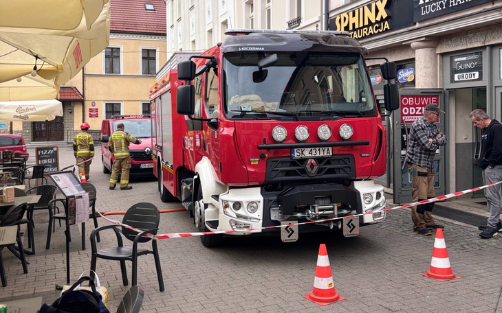 Wóz strażacki na ulicy, w tle strażacy i zabezpieczenia.