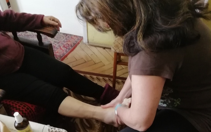 Kobieta masuje stopę innej osoby w domowym otoczeniu.