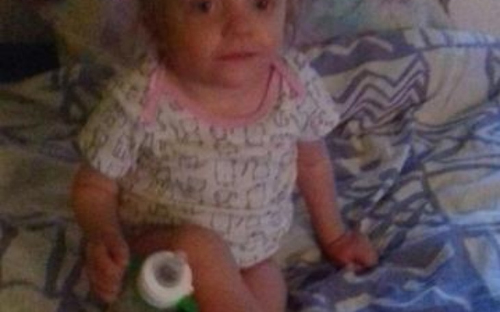 Dziecko siedzące na łóżku, trzyma butelkę.