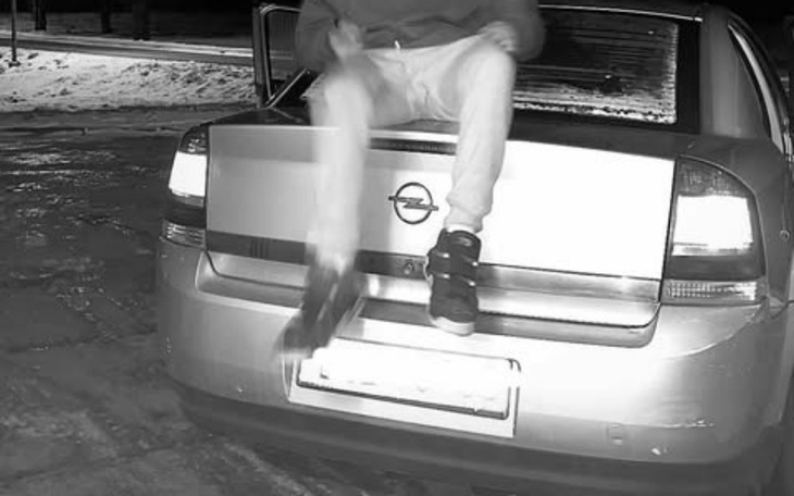 Osoba siedząca na tylnej klapie samochodu, w nocy na zaśnieżonej ulicy.