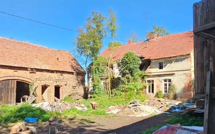 Zarośnięty dziedziniec z ruinami, w tle stare budynki.