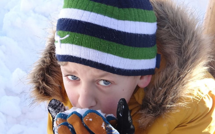 Chłopiec w zimowej czapce, jedzący śnieg.