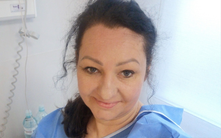 Kobieta w szpitalnym ubraniu, uśmiechająca się do kamery.