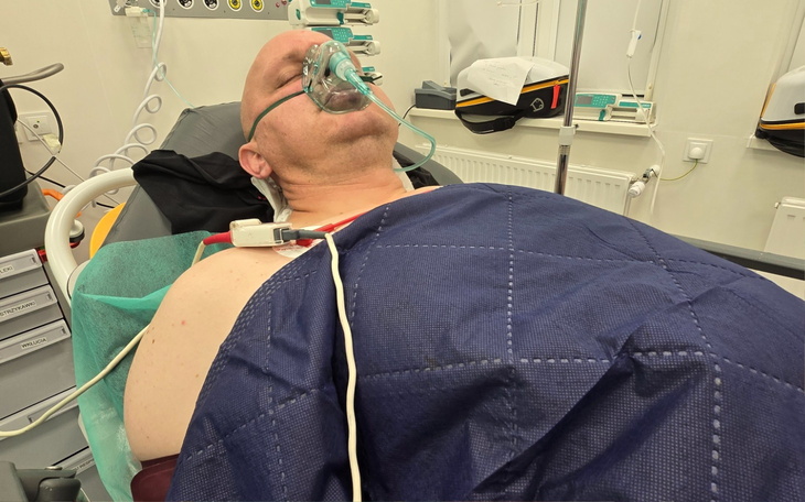 Mężczyzna w szpitalu z maską tlenową, leżący na łóżku szpitalnym.