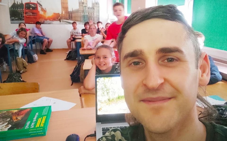 Nauczyciel z uczniami w klasie, uśmiechnięte twarze i laptop na biurku.