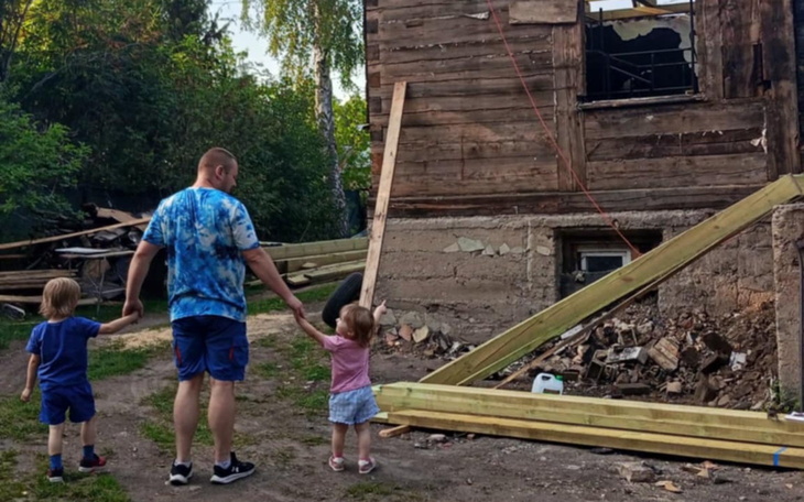 Dzieci trzymają się za ręce, stojąc przed zniszczonym budynkiem.