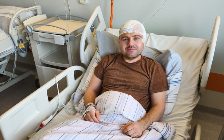 Mężczyzna w szpitalnym łóżku, z opatrunkiem na głowie.