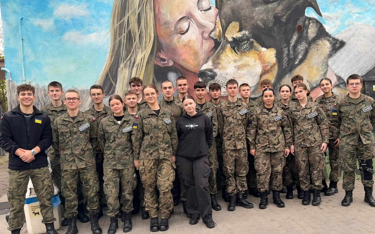 Grupa młodych ludzi w mundurach wojskowych przed muralem.