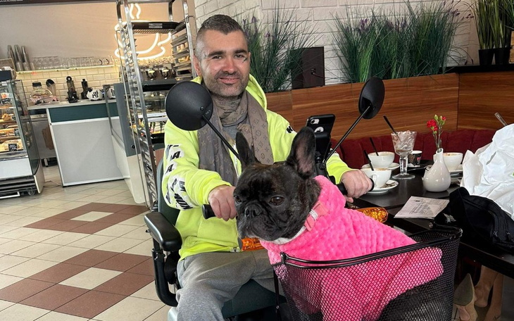 Mężczyzna w wózku inwalidzkim z psem w różowym sweterku w kawiarni.