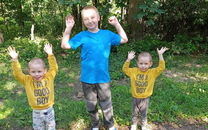 Trzech chłopców w lesie, podnoszą ręce w górę.