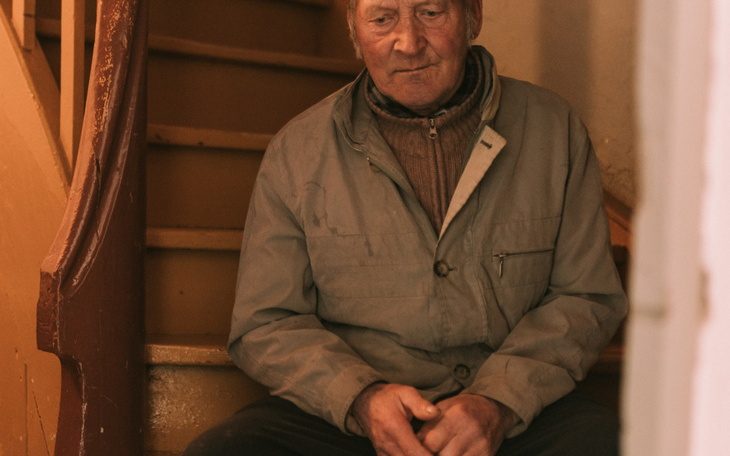 Starszy mężczyzna siedzący na schodach, z zamyśloną miną.