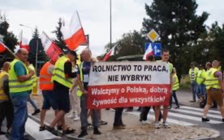 Protest rolników z transparentem, flagi Polski w tle.