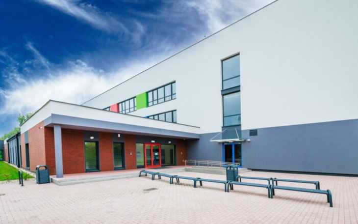 Nowoczesny budynek z dużymi oknami i przestrzenią przed wejściem.