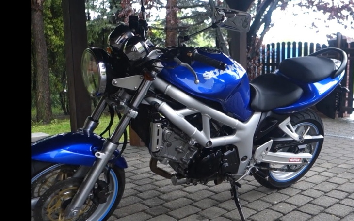 Motocykl w niebieskim kolorze, zaparkowany na kostce brukowej.