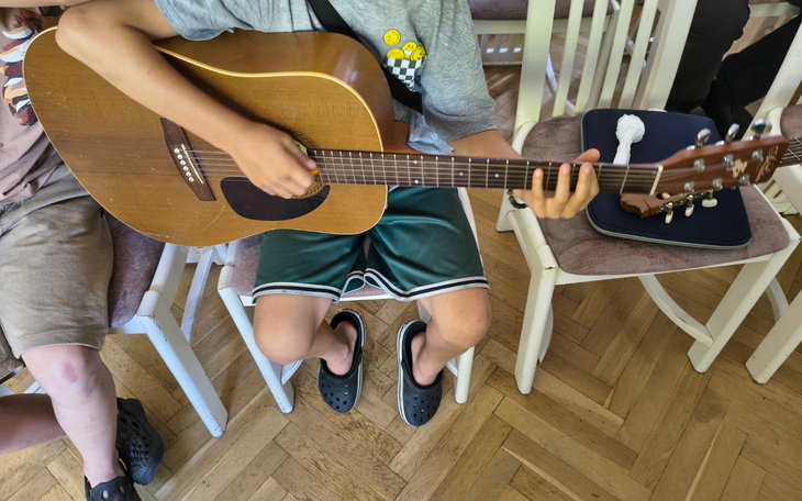 Chłopiec grający na gitarze w towarzystwie innych dzieci.