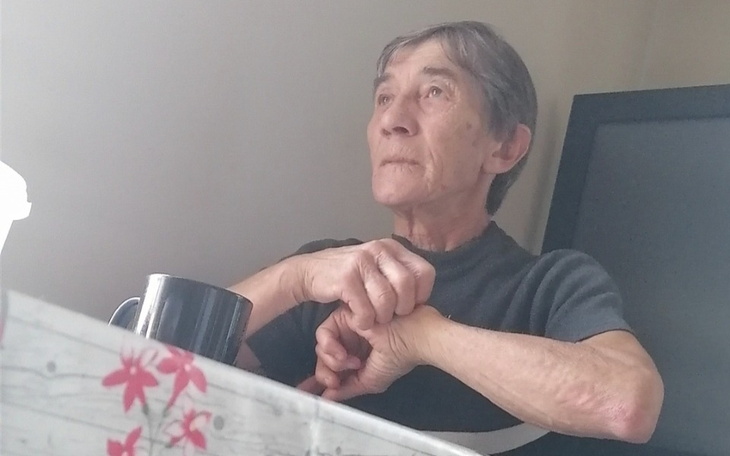 Starsza kobieta siedzi przy stole, zamyślona i patrzy w dal.