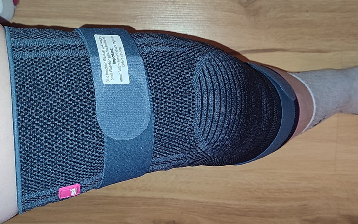 Zdjęcie kolana w ortezie, z widocznymi oznaczeniami na materiale.