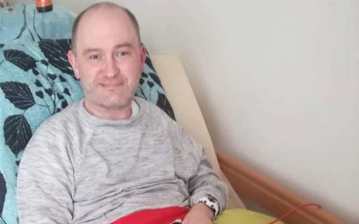 Mężczyzna w łóżku, uśmiechający się, w domowym otoczeniu.