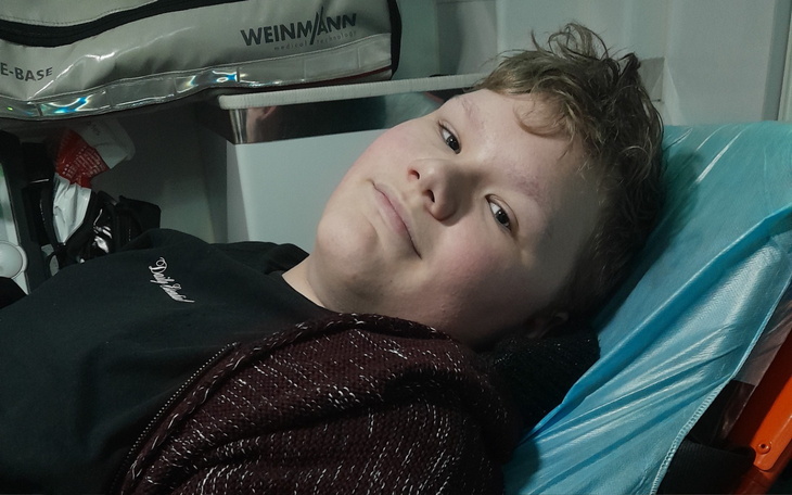 Chłopiec leżący na łóżku, uśmiechający się do kamery.
