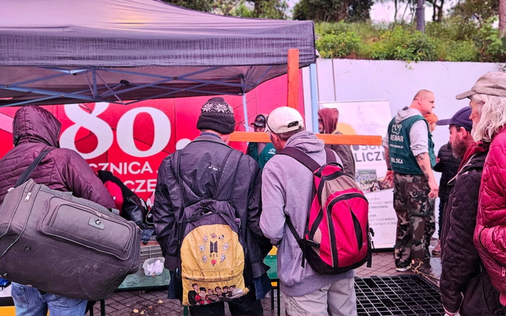 Grupa ludzi w kolejce przy stoisku charytatywnym.