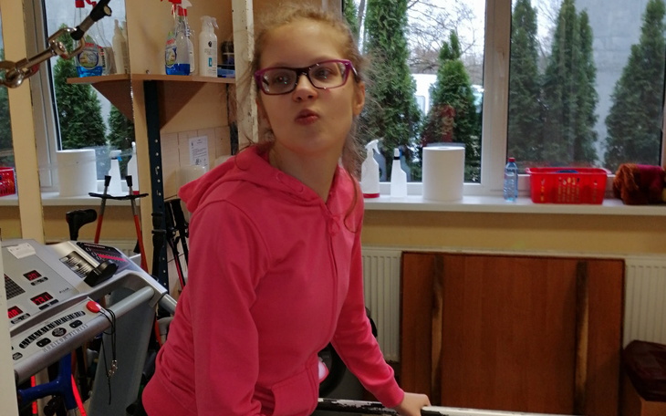 Młoda dziewczyna w różowej bluzie, ćwiczy w rehabilitacji.