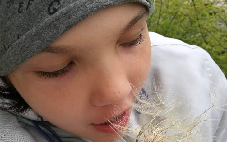 Dziecko w białej kurtce, wpatrzone w dmuchawce.