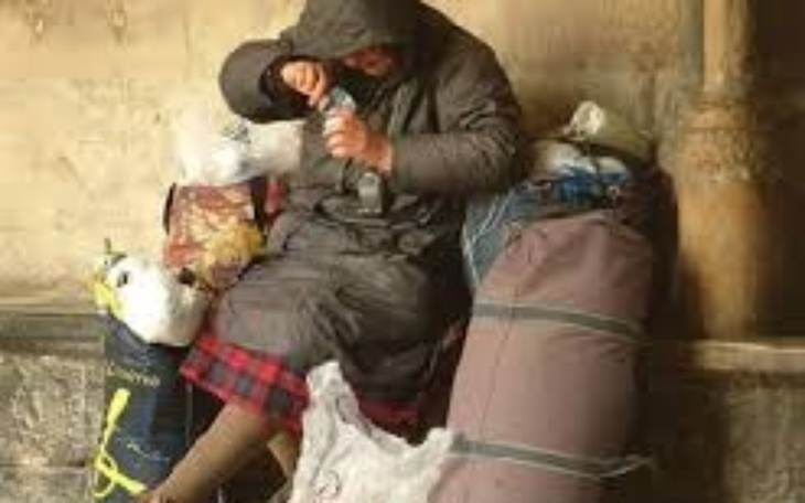 Osoba w szarej kurtce, przeszukująca torby w poszukiwaniu jedzenia.