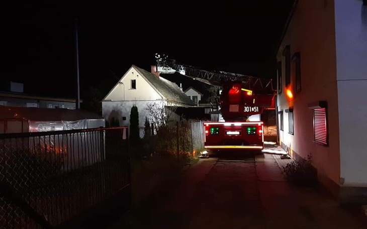 Wóz strażacki przy budynku w nocy, z włączonymi światłami.