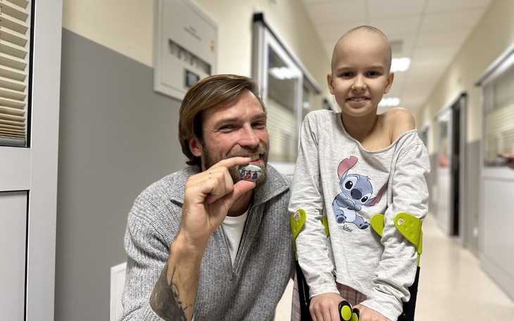 Uśmiechnięty mężczyzna z dzieckiem w szpitalnym korytarzu.