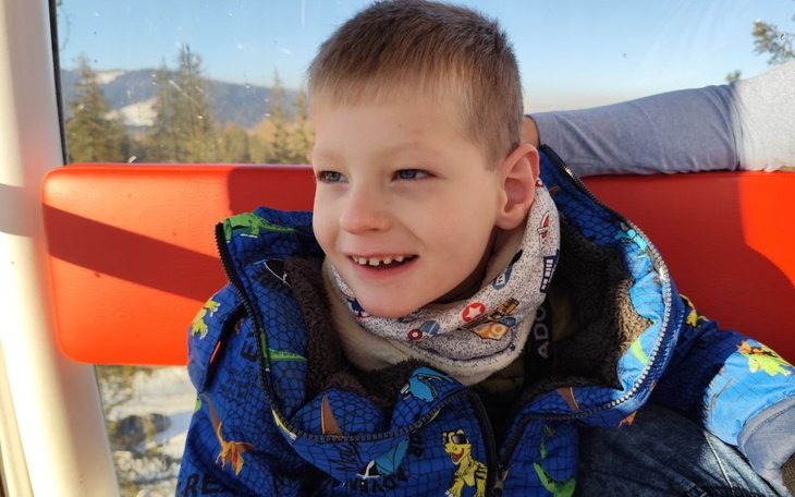 Chłopiec w kolorowej kurtce, uśmiechający się w gondoli.