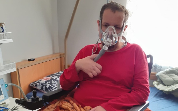 Mężczyzna w czerwonej koszulce z maską tlenową, siedzący w fotelu.