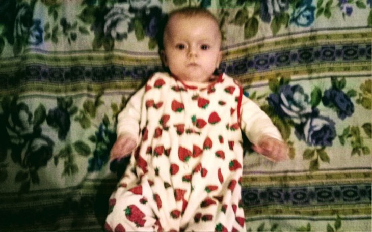 Małe dziecko w ubranku w truskawki leżące na kocu.