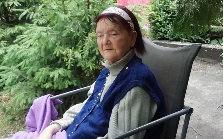 Starsza kobieta siedzi na tarasie, z zamyślonym wyrazem twarzy.