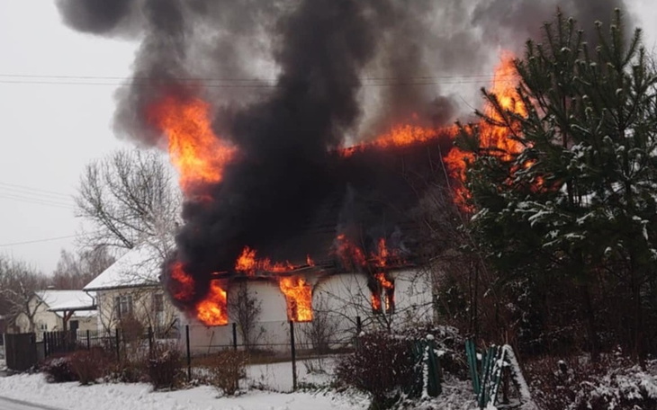 Płonący dom z dużym dymem w zimowej scenerii.